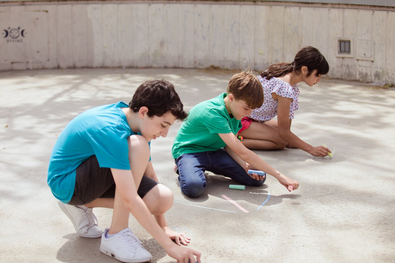Kids enjoying creative chalk drawing on a sunny day outside.